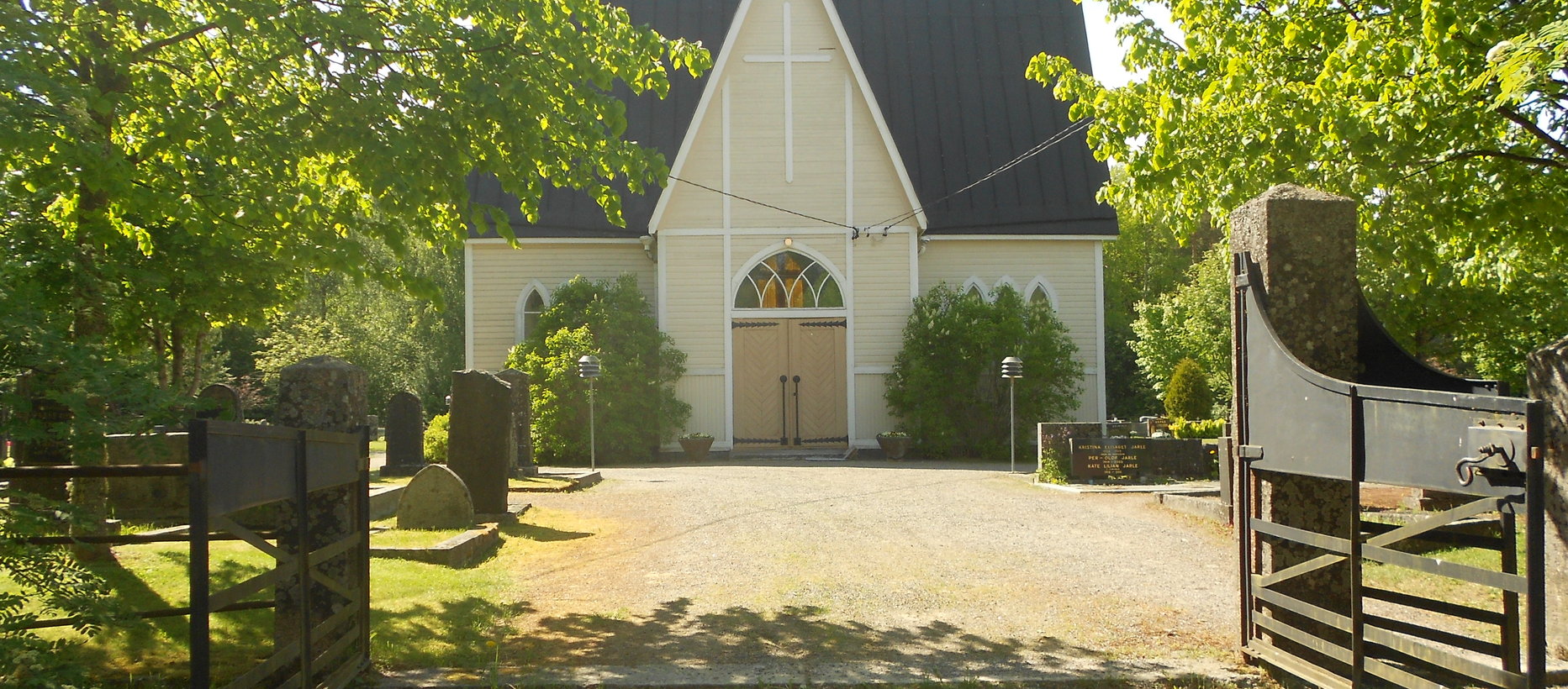 Kesäinen kuva portistra katsottuna pienestä korkeasta, valkoisesta kappelista.